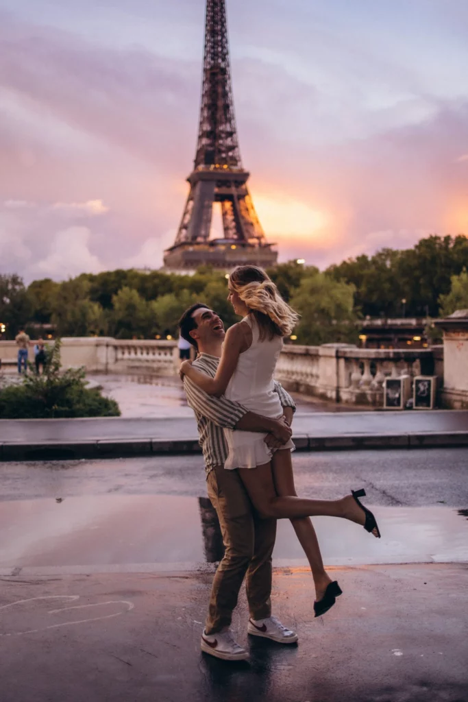 Sunset Eiffel Tower photoshoot of a couple, the man lifting his laughing partner on the wet stone of Trocadéro as the sky glows pink behind the tower