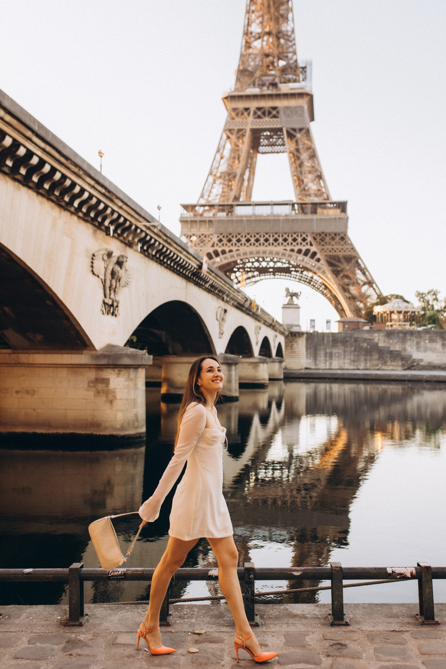 A joyful solo photoshoot along the Seine in Paris, walking past a stone arch bridge with the Eiffel Tower reflected in the river. Photographed by Julia Litvin, litvinphoto.com.